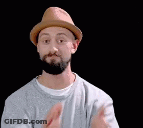 A Man With A Beard Wearing A Hat And A White Shirt Is Clapping His Hands . GIF