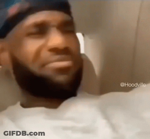 A Man With A Beard Wearing A Hat And A White Shirt Is Sitting In A Chair . GIF