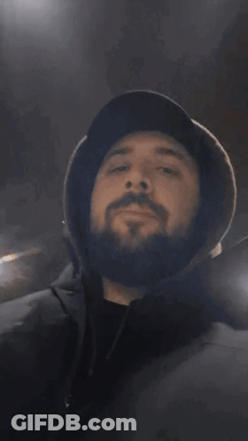 A Man With A Beard Wearing A Hat Covering His Mouth With His Hands GIF
