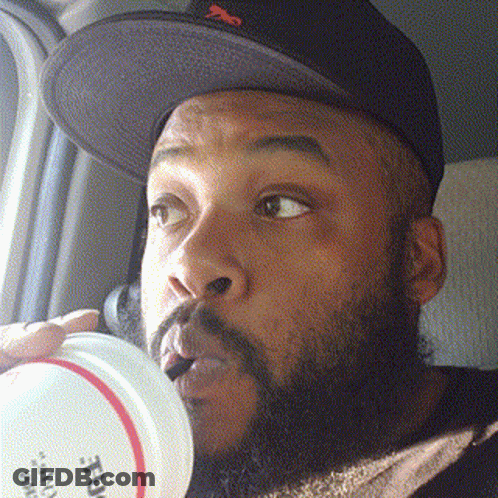 A Man With A Beard Wearing A Hat Is Drinking From A Container That Says ' True ' On It GIF