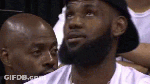 A Man With A Beard Wearing A Hat Is Sitting In A Stadium . GIF