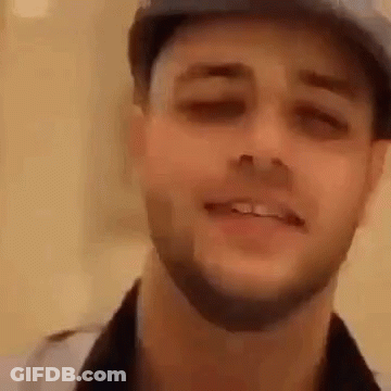 A Man With A Beard Wearing A Hat Is Smiling . GIF