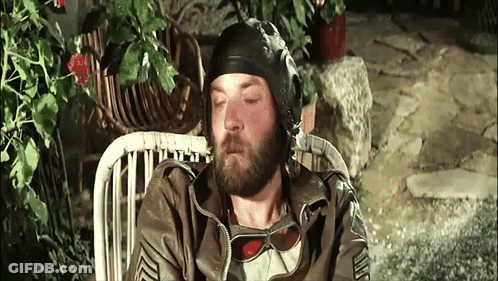 A Man With A Beard Wearing A Helmet And Sunglasses Is Sitting In A Chair GIF