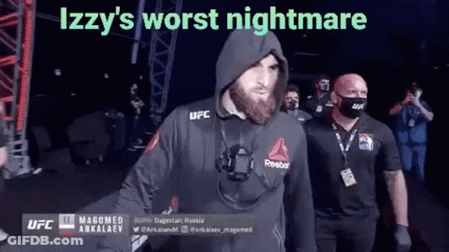 A Man With A Beard Wearing A Hooded Jacket And A Mask Is Walking Into A Ring . GIF