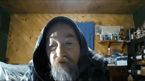 A Man With A Beard Wearing A Hooded Jacket Looks At The Camera GIF