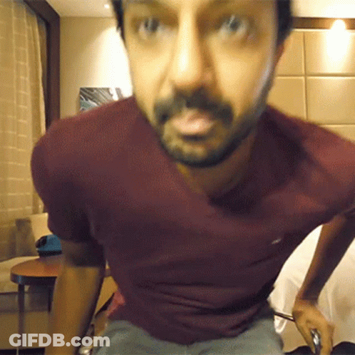 A Man With A Beard Wearing A Maroon Shirt Looks At The Camera GIF