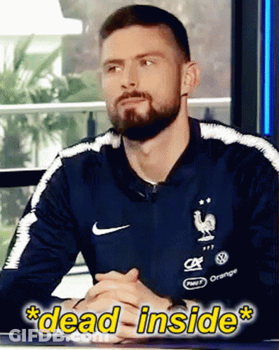 A Man With A Beard Wearing A Nike Shirt Is Sitting At A Table With His Hands Folded GIF