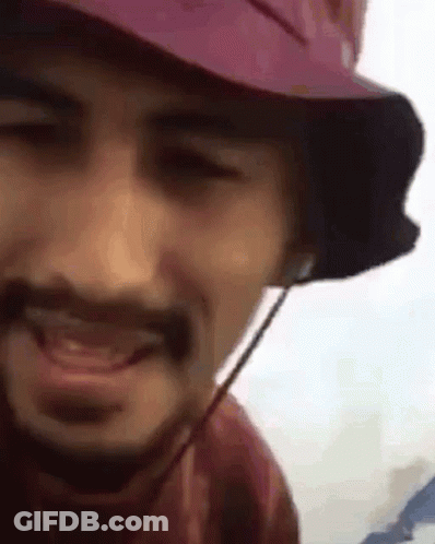 A Man With A Beard Wearing A Pink Hat And Headphones Is Smiling . GIF