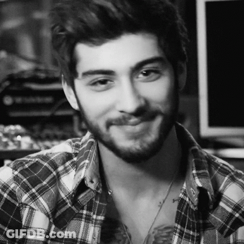 A Man With A Beard Wearing A Plaid Shirt Is Smiling In A Black And White Photo GIF