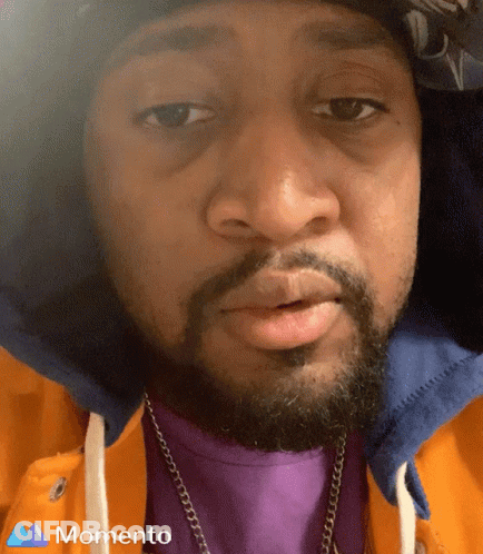 A Man With A Beard Wearing A Purple Shirt And A Momento Logo On The Bottom GIF