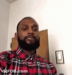 A Man With A Beard Wearing A Red And Black Plaid Shirt Is Standing In A Room . GIF