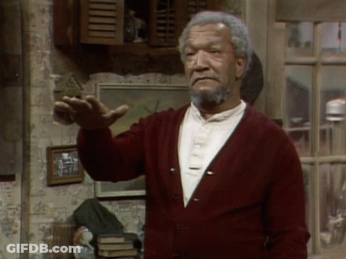 A Man With A Beard Wearing A Red Cardigan Is Standing In Front Of A Window GIF