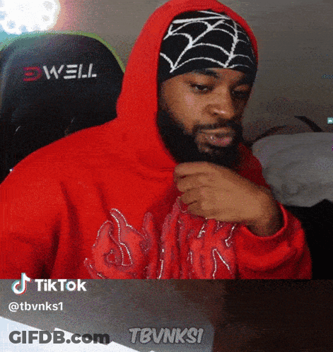A Man With A Beard Wearing A Red Hoodie And A Black And White Spider Web Hat GIF