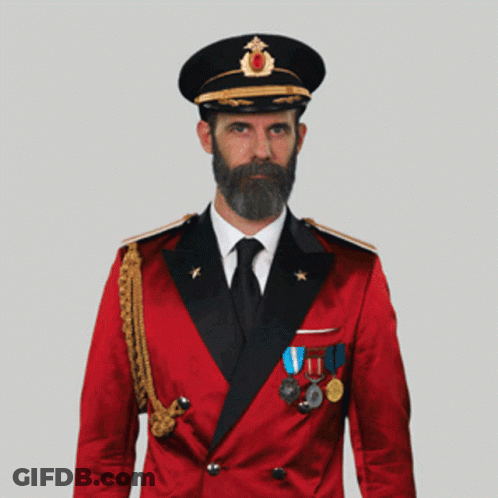 A Man With A Beard Wearing A Red Suit And Black Hat Salutes GIF