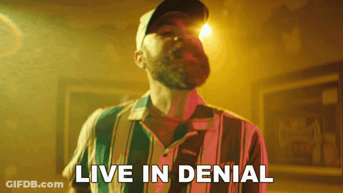 A Man With A Beard Wearing A Striped Shirt And A Hat Says Live In Denial GIF