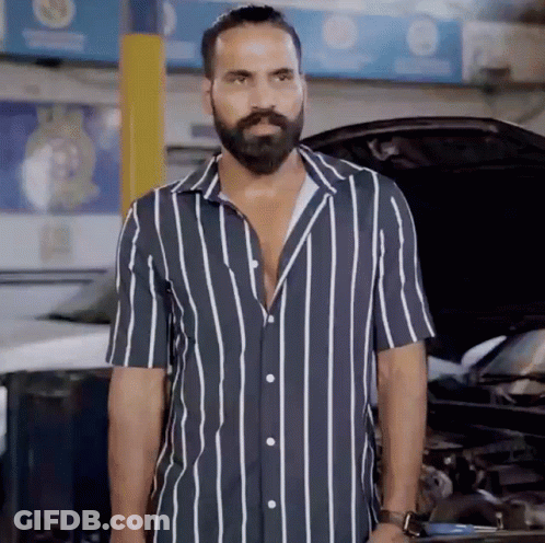 A Man With A Beard Wearing A Striped Shirt Stands In Front Of A Car GIF