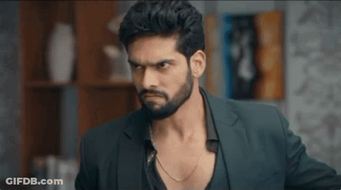 A Man With A Beard Wearing A Suit And A Chain Around His Neck Is Looking At The Camera . GIF
