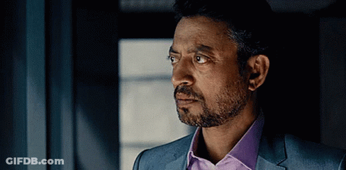 A Man With A Beard Wearing A Suit And A Purple Shirt Is Looking Out A Window . GIF