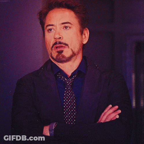 A Man With A Beard Wearing A Suit And Tie Has His Arms Crossed GIF