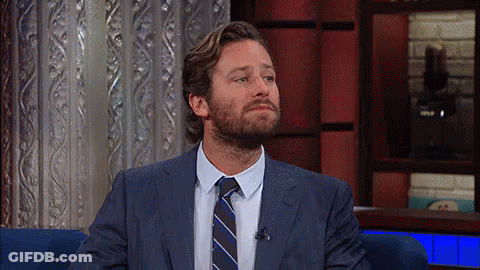 A Man With A Beard Wearing A Suit And Tie Is Sitting In A Chair . GIF