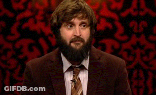 A Man With A Beard Wearing A Suit And Tie Is Standing In Front Of A Red Wall . GIF