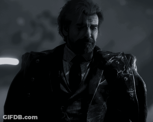 A Man With A Beard Wearing A Suit And Tie Is Standing In The Dark GIF