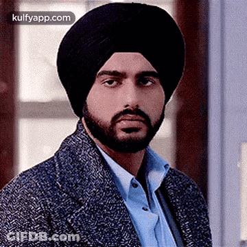 A Man With A Beard Wearing A Turban And A Jacket Is Looking At The Camera . GIF