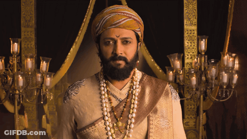 A Man With A Beard Wearing A Turban And Pearls Looks At The Camera GIF