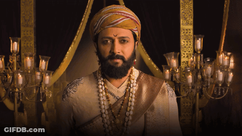A Man With A Beard Wearing A Turban And Pearls Looks At The Camera GIF