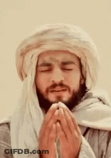 A Man With A Beard Wearing A Turban Is Praying With His Eyes Closed . GIF