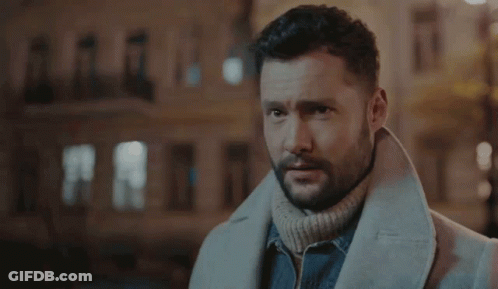 A Man With A Beard Wearing A White Coat And A Turtleneck Sweater . GIF