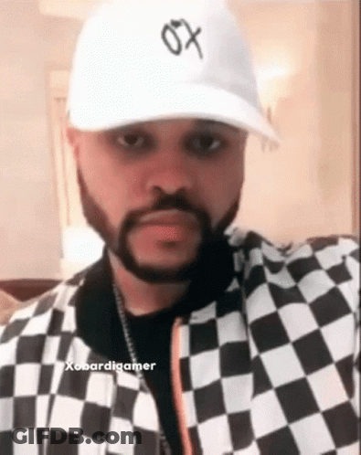 A Man With A Beard Wearing A White Hat And A Black And White Checkered Jacket . GIF