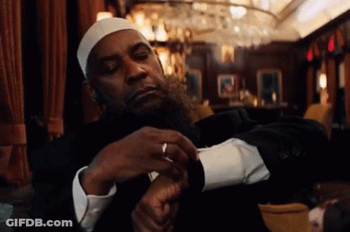 A Man With A Beard Wearing A White Hat And A Black Suit Is Looking At His Watch GIF