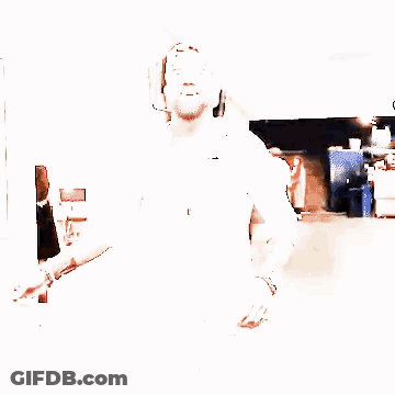 A Man With A Beard Wearing A White Shirt And A Baseball Cap Is Walking Down A Hallway . GIF