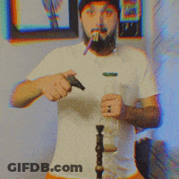 A Man With A Beard Wearing A White Shirt And A Black Hat Smoking A Cigarette GIF
