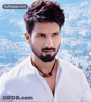 A Man With A Beard Wearing A White Shirt And A Necklace Is Looking At The Camera . GIF