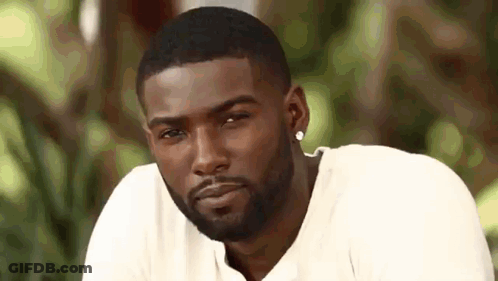 A Man With A Beard Wearing A White Shirt And Earrings Is Looking At The Camera . GIF