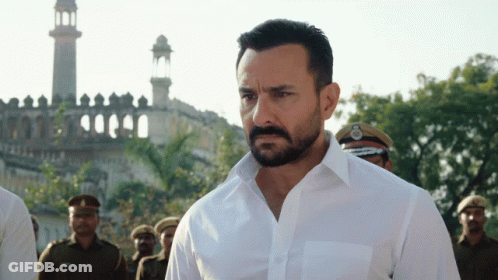 A Man With A Beard Wearing A White Shirt Is Standing In Front Of A Mosque GIF