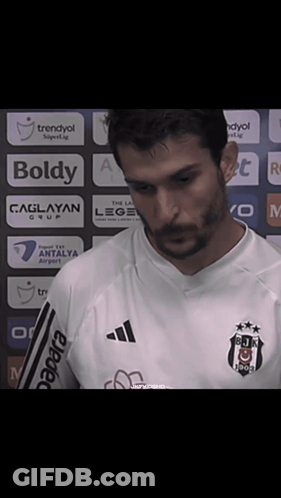 A Man With A Beard Wearing A White Shirt That Says Boldy On It GIF