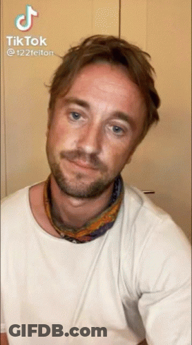A Man With A Beard Wearing A White T-Shirt And A Scarf Around His Neck GIF
