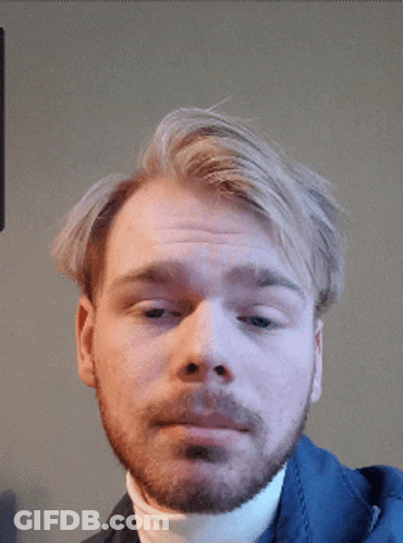 A Man With A Beard Wearing A White Turtleneck Looks At The Camera GIF