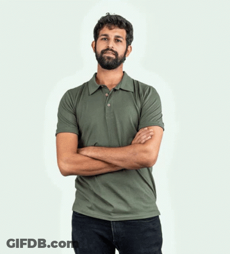 A Man With A Beard Wearing A Yellow Polo Shirt With His Hands In His Pockets GIF