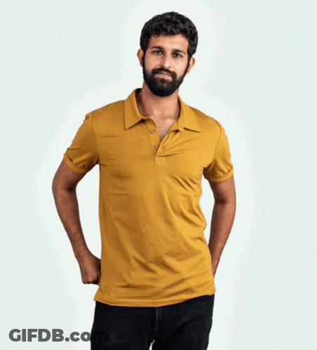 A Man With A Beard Wearing A Yellow Polo Shirt With His Hands In His Pockets GIF