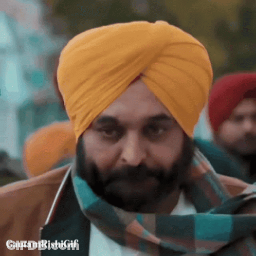 A Man With A Beard Wearing A Yellow Turban And A Green Scarf GIF