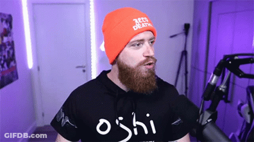 A Man With A Beard Wearing An Orange Beanie And A Black Shirt That Says Oshi GIF