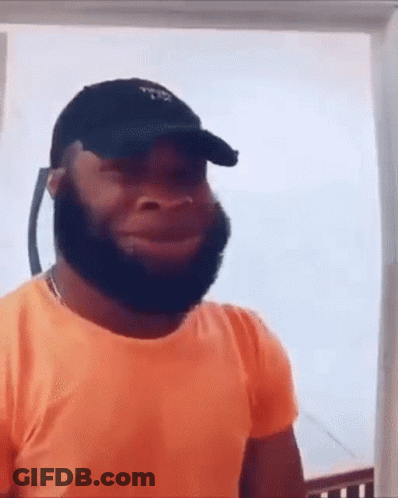 A Man With A Beard Wearing An Orange Shirt And A Black Hat . GIF