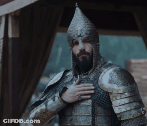 A Man With A Beard Wearing Armor And A Helmet With His Hand On His Chest GIF