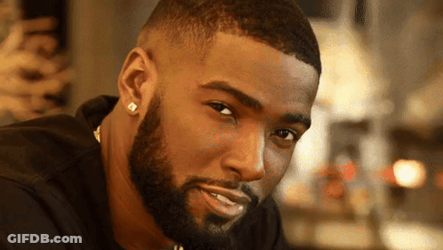 A Man With A Beard Wearing Earrings And A Black Shirt GIF