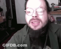 A Man With A Beard Wearing Glasses And A Green Jacket Is Talking . GIF