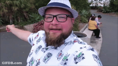 A Man With A Beard Wearing Glasses And A Hat With A Shirt With Cars On It GIF